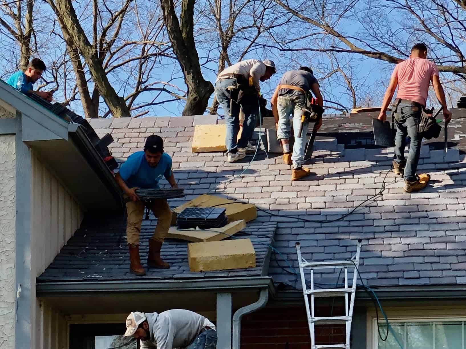 Roofing crew installing shingles on house roof, professional roofing and construction services.