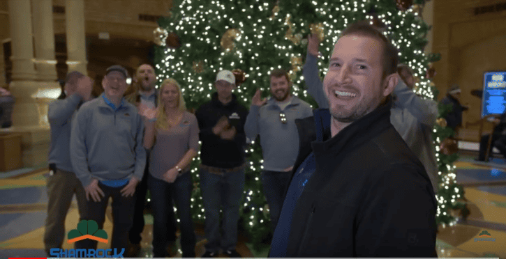Christmas celebration with Shamrock Roofing team in front of a decorated Christmas tree in a festive office environment.