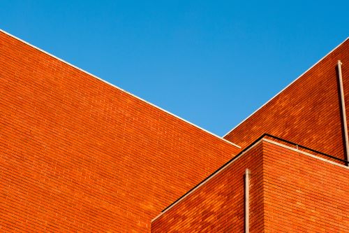 Bright red brick building with clear blue sky, showcasing roofing and construction services.