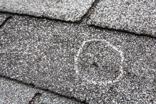 Weathered asphalt shingles with a hail dent and powdery snow coating, showcasing durable roof materials.