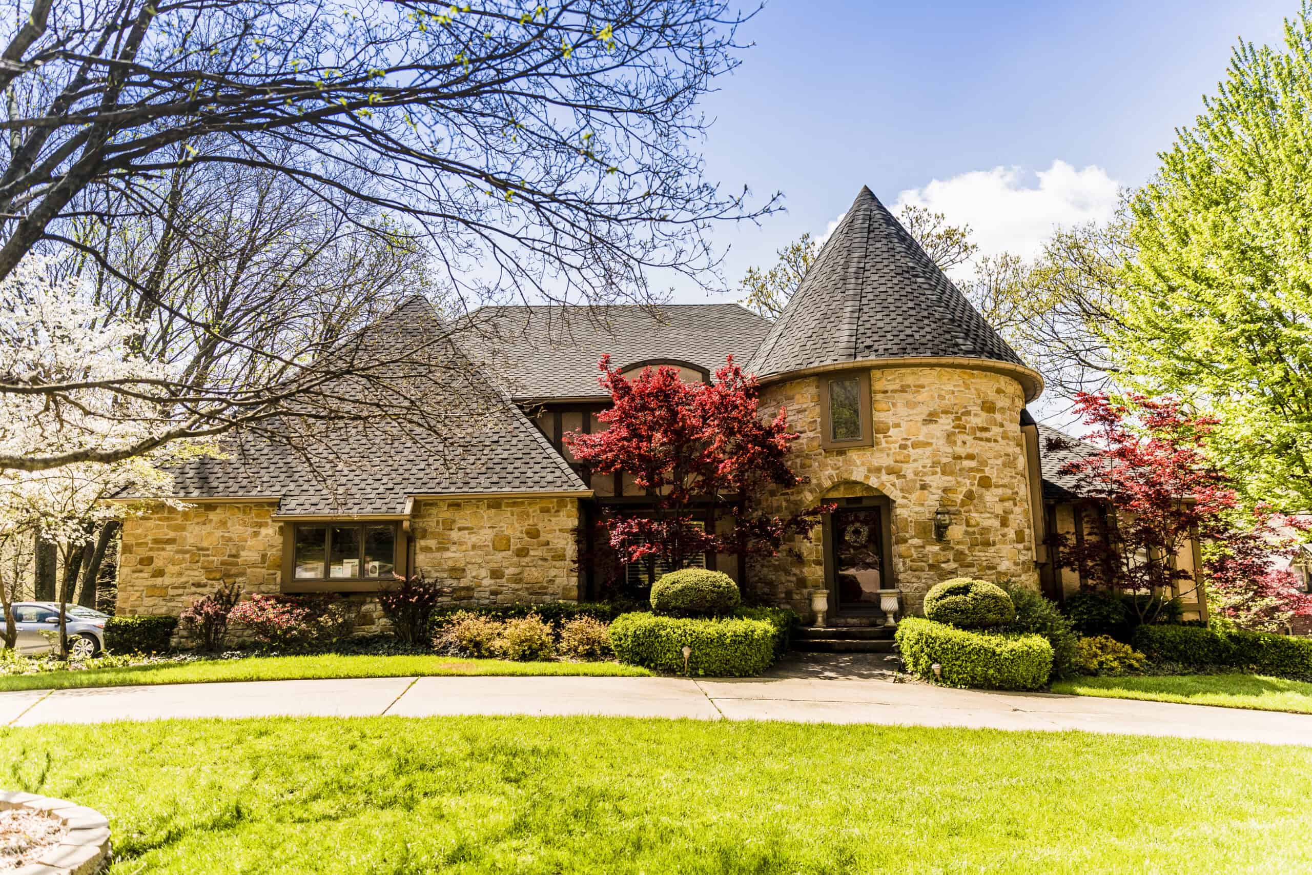 Elegant stone house with slate roof, surrounded by lush greenery and flowering trees, showcasing expert roofing and construction services.