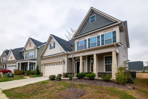 Two-story new residential homes with siding, front yard, and landscaping in a suburban neighborhood.