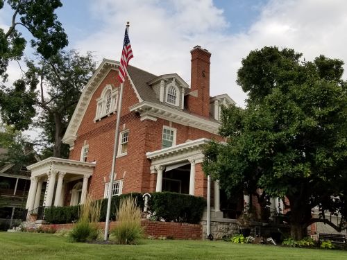Traditional brick house with American flag, surrounded by lush greenery, showcasing expert roofing and construction services.
