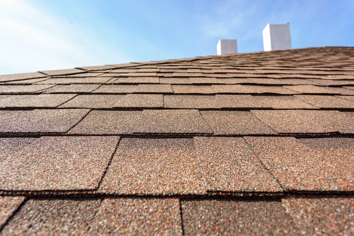 close up view of brown asphalt shingles on roof with blue sky in background