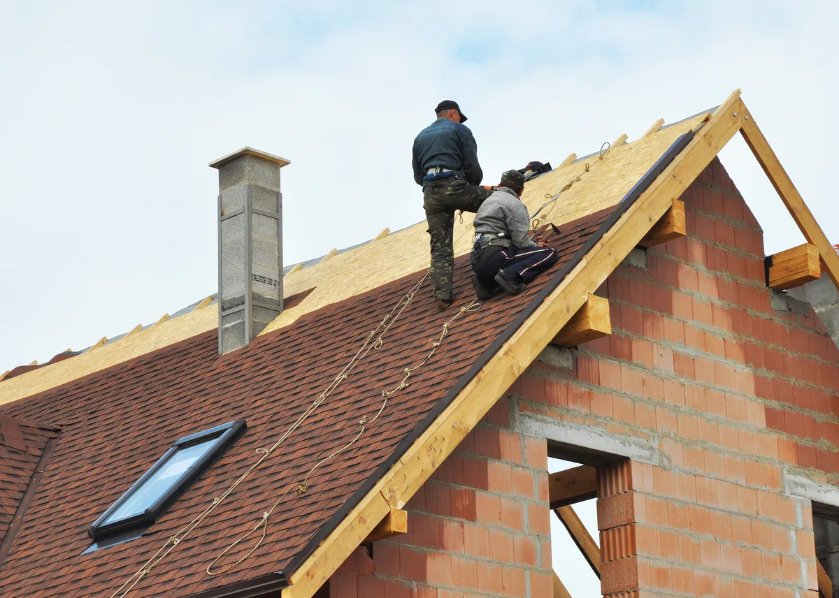 two male workers installing asphalt shingles on residential roof