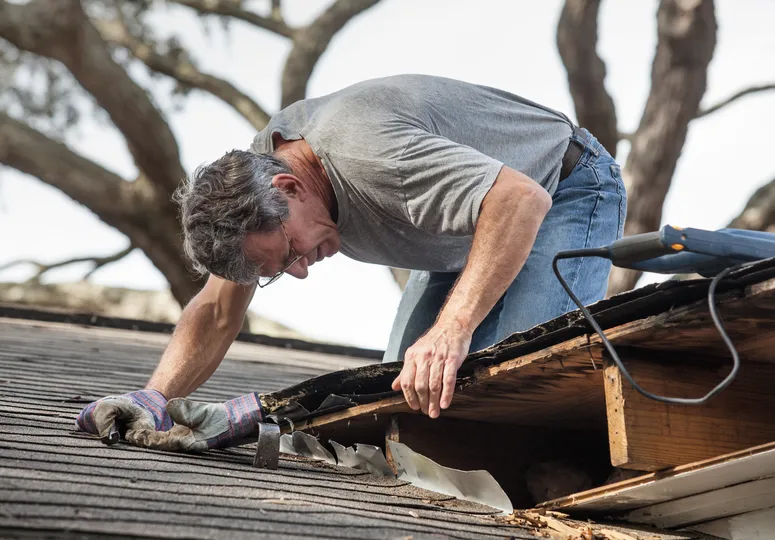 man on asphalt shingle roof making repairs to eave