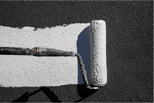 Bright white roof paint being applied with a roller on a textured black roof surface.
