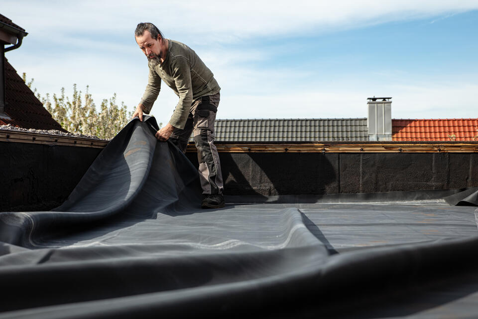 how to seal a flat roof-man on a flat roof applying roofing materials