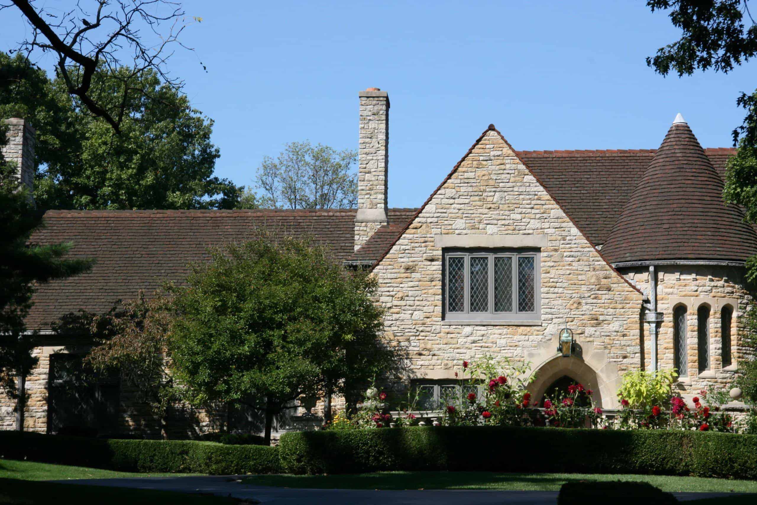 Stately stone house with a lush green front yard and classic roofing, showcasing expert roofing and construction services.
