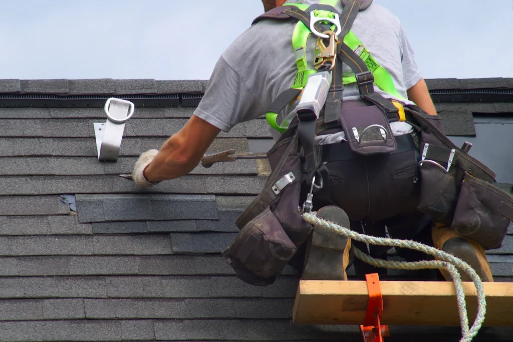 roofing contractor wearing a harness while repairs a section of a shingled roof