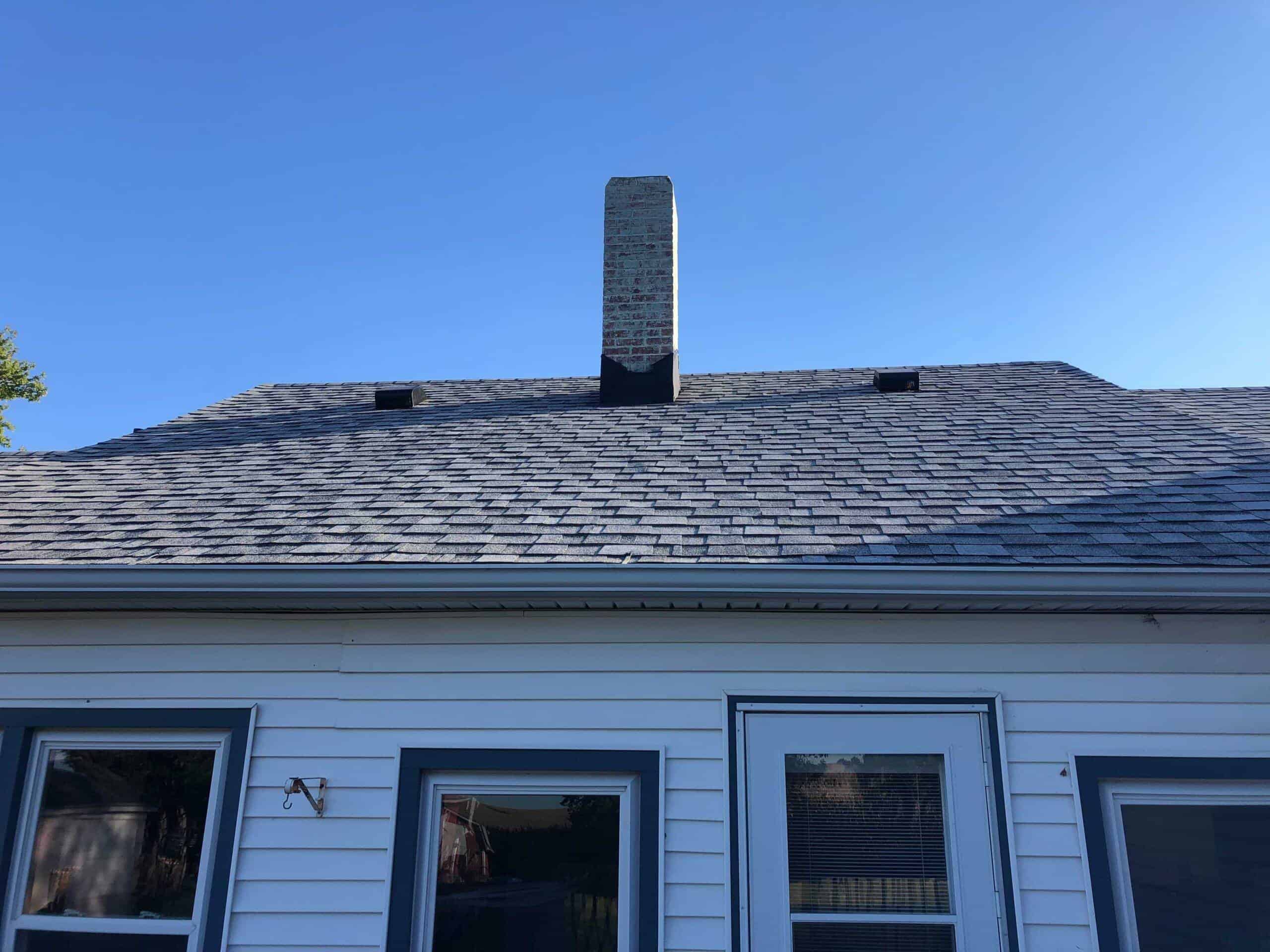 Weather-resistant asphalt shingle roof with brick chimney on a residential home.
