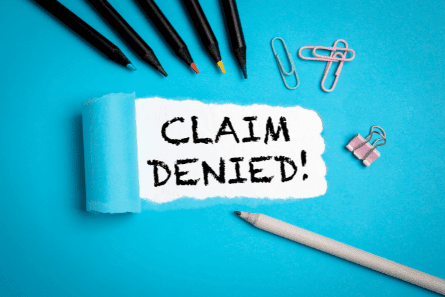 Insurance claim denial notice with office supplies and a "Claim Denied" sign.