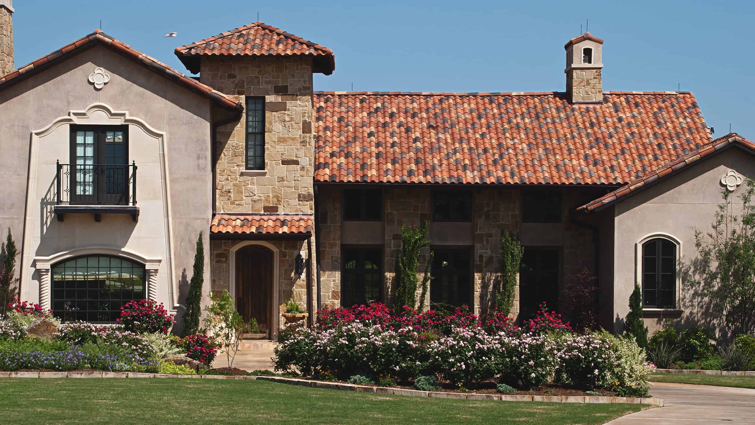 Stylish stone and stucco house with Mediterranean roof tiles, lush garden, and well-maintained landscaping.