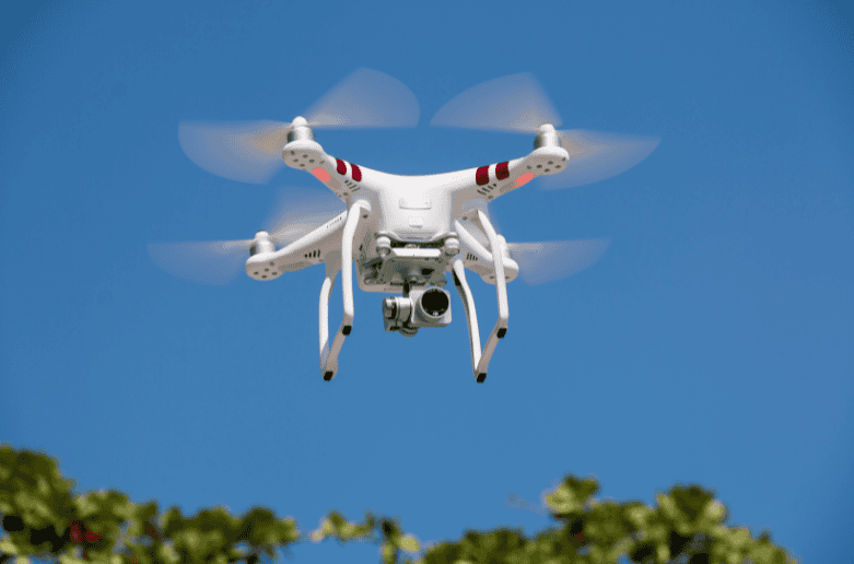 Uav drone flying outdoors against blue sky with trees in background.