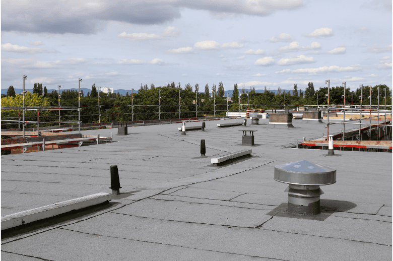 Shamrock roofing flat roof with vents and safety railing in cityscape environment.