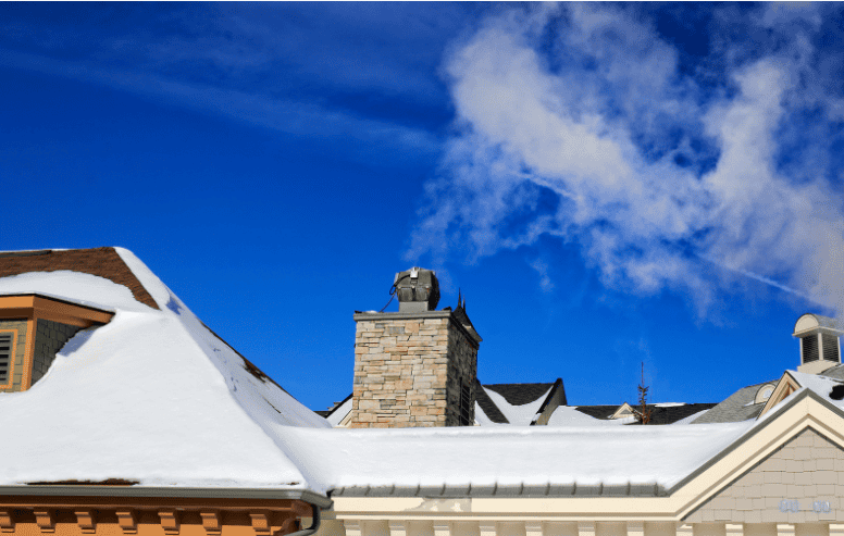 Snow-covered roof with chimney and blue sky, showcasing professional roofing and construction services.