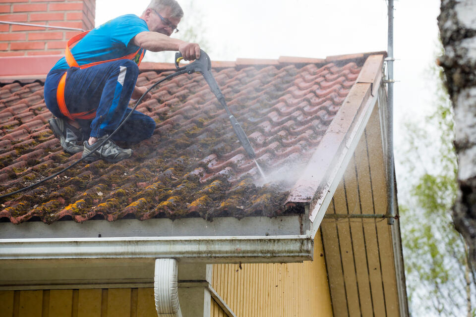 how to remove mold from roof shingles-man wearing a safety harness power washing roof shingles