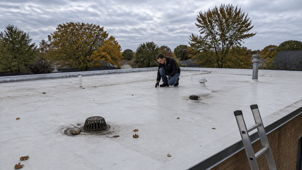 Roofing worker inspecting PVC roofing maintenance before winter on a commercial roof in Kansas